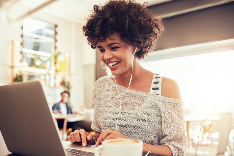 Image of happy woman using laptop while sitting at cafe. Young african american woman sitting in a coffee shop and working on laptop.