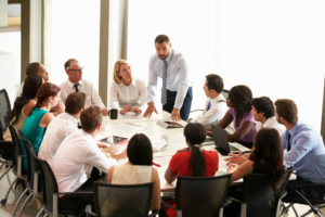 Businessman Addressing Colleagues In Meeting Around Boardroom Table